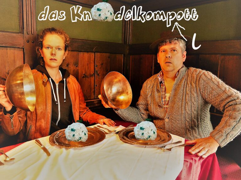 Das Bild zeigt ein Poster mit der Aufschrift "Knödelkompott" auf dem ein Mann und eine Frau einen Knödel auf einem Teller vor sich stehen haben